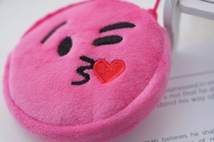 Close-up of pink round plush coin purse with embroidered heart and kissing emoji face