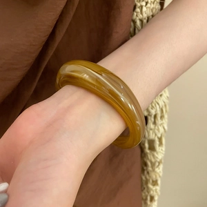 Nahaufnahme der bernsteinfarbenen Acryl-Armspange am Handgelenk in warmen Erdtönen