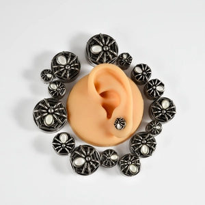 Detailed view of silver spider ear plugs showing multiple size options and fit on ear model