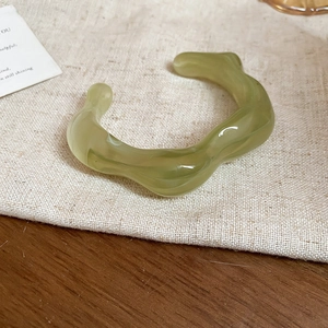 Detail view of a translucent green wavy resin bangle on a minimalist linen background