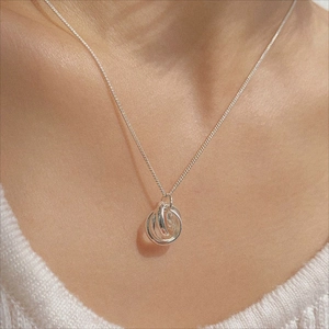 Detail of three interlocking silver rings necklace worn on a woman's neck
