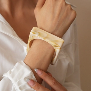 Close-up of a wide square acrylic bangle with cream marble pattern on a woman's wrist
