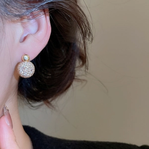 Detailed close-up of a gold-plated spherical stud earring with shimmering pavé zircon stones