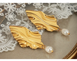 Détail de boucles d'oreilles feuille dorée avec perle blanche sur fond de dentelle