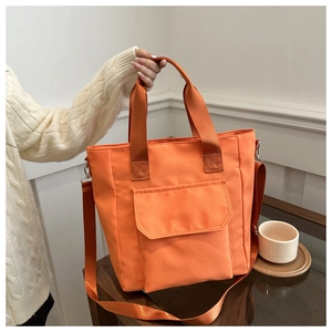 Detail of the orange nylon tote bag showing adjustable straps and front flap pocket