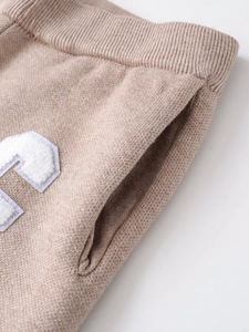Detail of khaki knitted pants showing ribbed waist, side pockets and bouclé letter patch