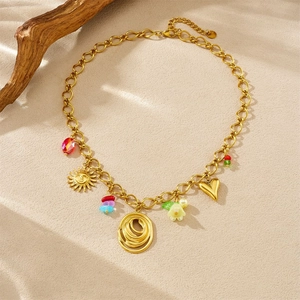 Flat lay of a gold charm necklace with colorful beads and flower pendants on sand