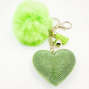Close-up of green faux fur pompom keychain with rhinestone heart and golden tassel