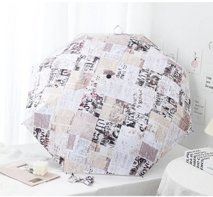 Detail of three-fold umbrella with vintage newspaper print on a white table
