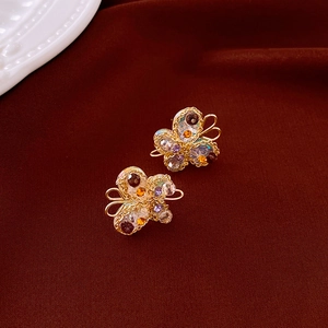 Detailed macro of golden wire butterfly earrings with purple crystals on red velvet