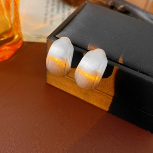 Macro view of minimalist silver square C-shaped earrings with textured brushed metal finish