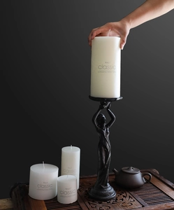 Detail showing hands placing a white pillar candle onto a vintage iron angel candle holder