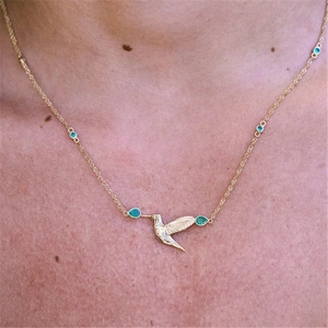 Detailed close-up of a hummingbird pendant necklace with green gemstones on a model