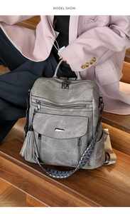 Detail of vintage grey PU backpack with woven strap and tassel on wooden stairs