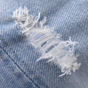 Macro shot of distressed blue denim fabric with vintage ripped details and white fiber texture