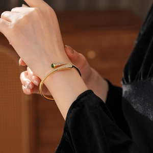 Detail of gold-plated open bangle with green gemstones and pavé zircon settings