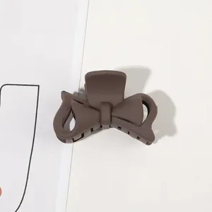 Detail of a matte dark brown bow-shaped shark hair claw clip on a minimalist surface
