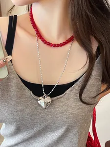 Close-up of a red bead necklace layered with a long silver chain and heart pendant