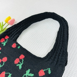 Detail of black knit tote bag featuring red cherry patterns and soft woven texture