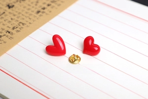 Detail of red heart pins with glossy finish and golden butterfly clasp on paper