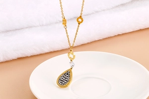 Macro shot of gold necklace with water-drop pendant, rhinestone inlay and Forever engraving