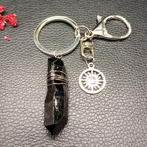 Detail of black crystal pillar keychain with silver sun charm on leather background