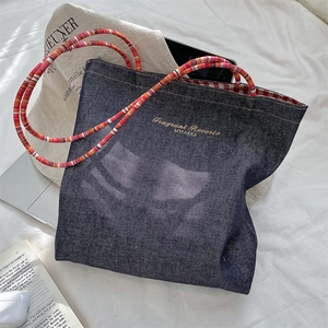 Detailed view of a retro denim tote bag featuring colorful braided handles and gold embroidery