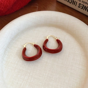 Elegante goldene Ohrringe mit roter Glasur auf beigem Keramikteller und rotem Stoff