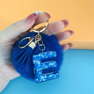 Close-up of blue pom pom keychain with gold hardware and glittery letter E pendant