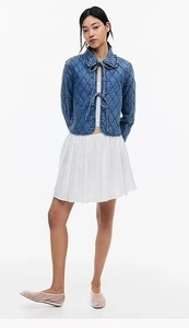 Detail of blue quilted jacket with tie-front bow design and white pleated skirt outfit