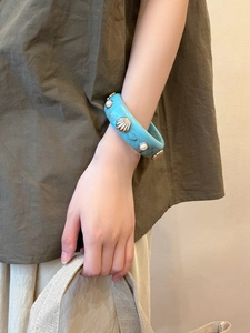 Close-up of a wide marble resin bangle with gold shell and pearl on model wrist