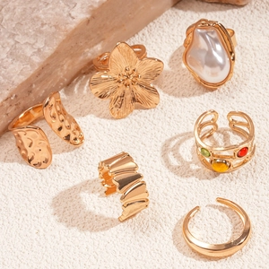 Golden 6-piece ring set with floral and pearl designs on natural stone background