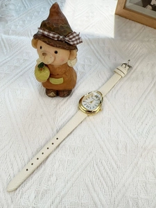 Detail of snake-head gold watch with Roman numerals on white leather strap
