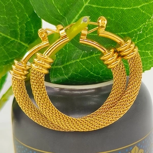 Close-up of golden mesh woven earrings hanging on green leaves with metal texture