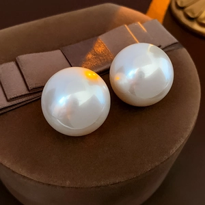 Macro shot of large round pearl stud earrings displayed on a brown velvet jewelry box