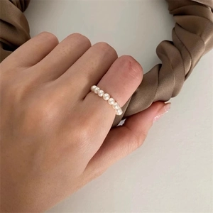 Close-up of minimalist white pearl chain ring on finger with silk fabric background