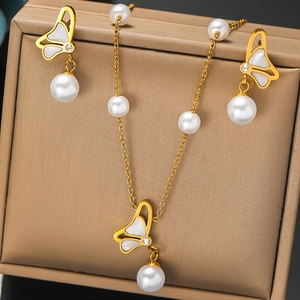 Détail d'un collier papillon doré et boucles d'oreilles perles dans une boîte à bijoux