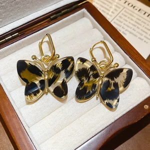 Detailed close-up of leopard print butterfly earrings on a premium wooden jewelry box tray