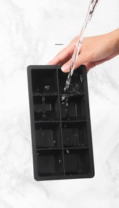 Gros plan d'un bac à glaçons en silicone noir flexible rincé sous l'eau courante