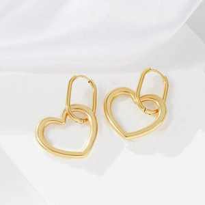 Detail view of gold hollow heart drop earrings on a white stand with silk fabric
