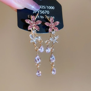 Macro detail of silver needle earrings featuring pink rhinestone flowers and crystal drops