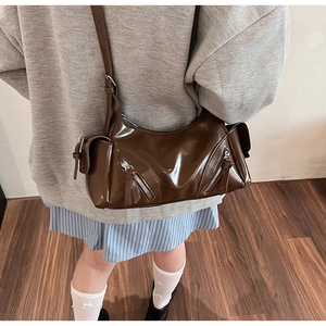 Detail of vintage brown patent leather crossbody bag with adjustable strap worn by model