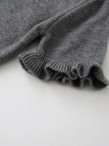 Detail shot of the ruffled cuff on a grey fine-knit sweater with delicate textures