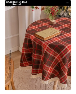 Detail of red and green plaid round tablecloth with beige fringe and holiday decor
