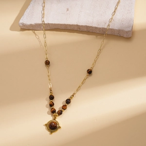 Close-up of vintage gold necklace with tiger eye beads and round engraved flower pendant