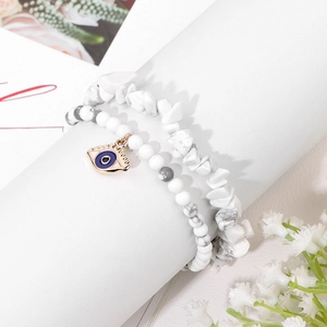 Detail of white stone bead bracelets with evil eye charm on a white display stand