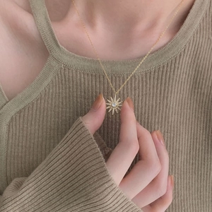 Detailed close-up of a gold sunburst star pendant with a center stone on a model