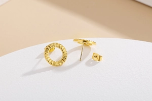 Macro detail of gold-plated geometric round studs with unique ripple texture finish