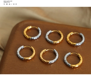 Macro detail of U-shaped gold and silver earrings with hammered texture on wooden base