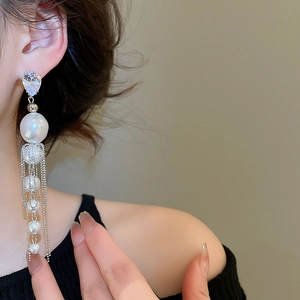 Détail de boucles d'oreilles à pompons argentées avec perles et cristaux sur modèle